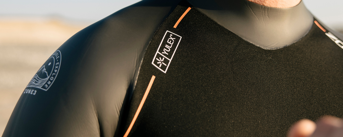 Close-up of a person wearing a wetsuit with a brand logo on a blurred beach background