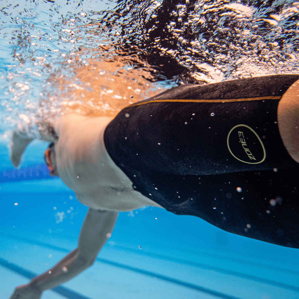 Vista submarina de un nadador con jammer MF-X negro y logotipo circular dorado, avanzando por la piscina