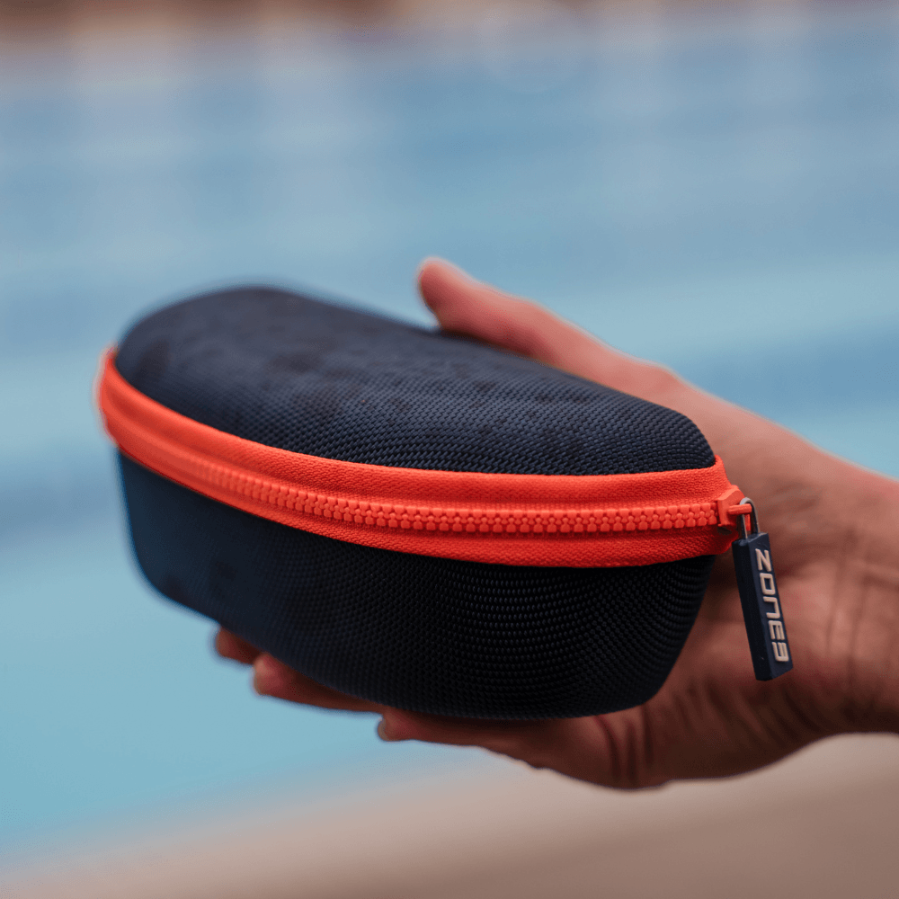 Estuche protector de gafas de natación en azul marino, con cremallera naranja vivo, sostenido en la mano.
