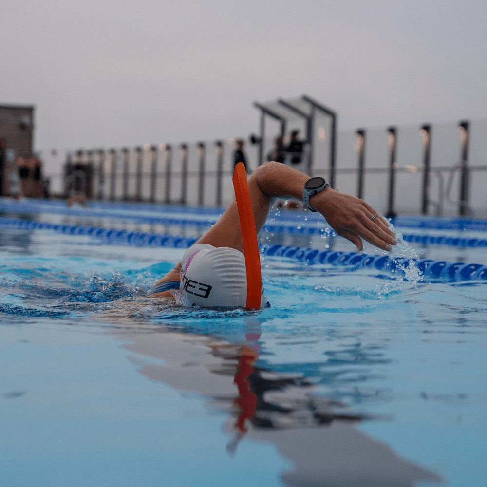 Nadador en la piscina con snorkel frontal naranja vivo, junto a las corcheras, con gorro blanco y gafas