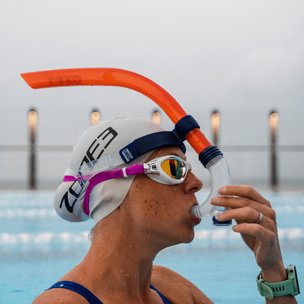 Nadador con gorro blanco, gafas de correa rosa y snorkel frontal naranja vivo durante un entrenamiento en piscina
