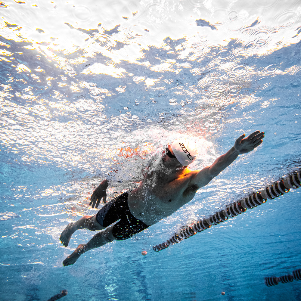 Swimmer in action underwater with a swim cap and goggles.