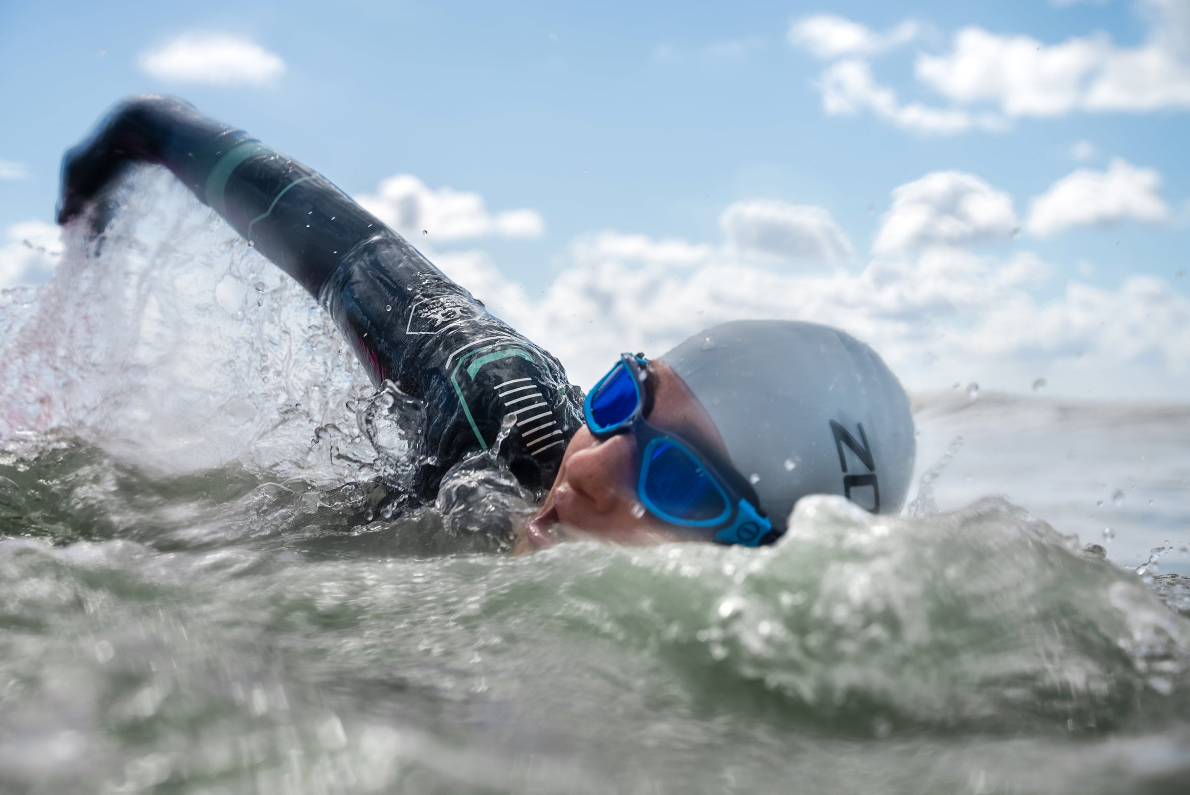 Person swimming in open water with a swim cap and goggles.