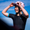 Mujer con el trisuit Activate+ de manga corta para mujer de ZONE3, ajustándose las gafas de sol sobre un casco rosa. El trisuit es negro, con puños de manga de color y cremallera frontal.