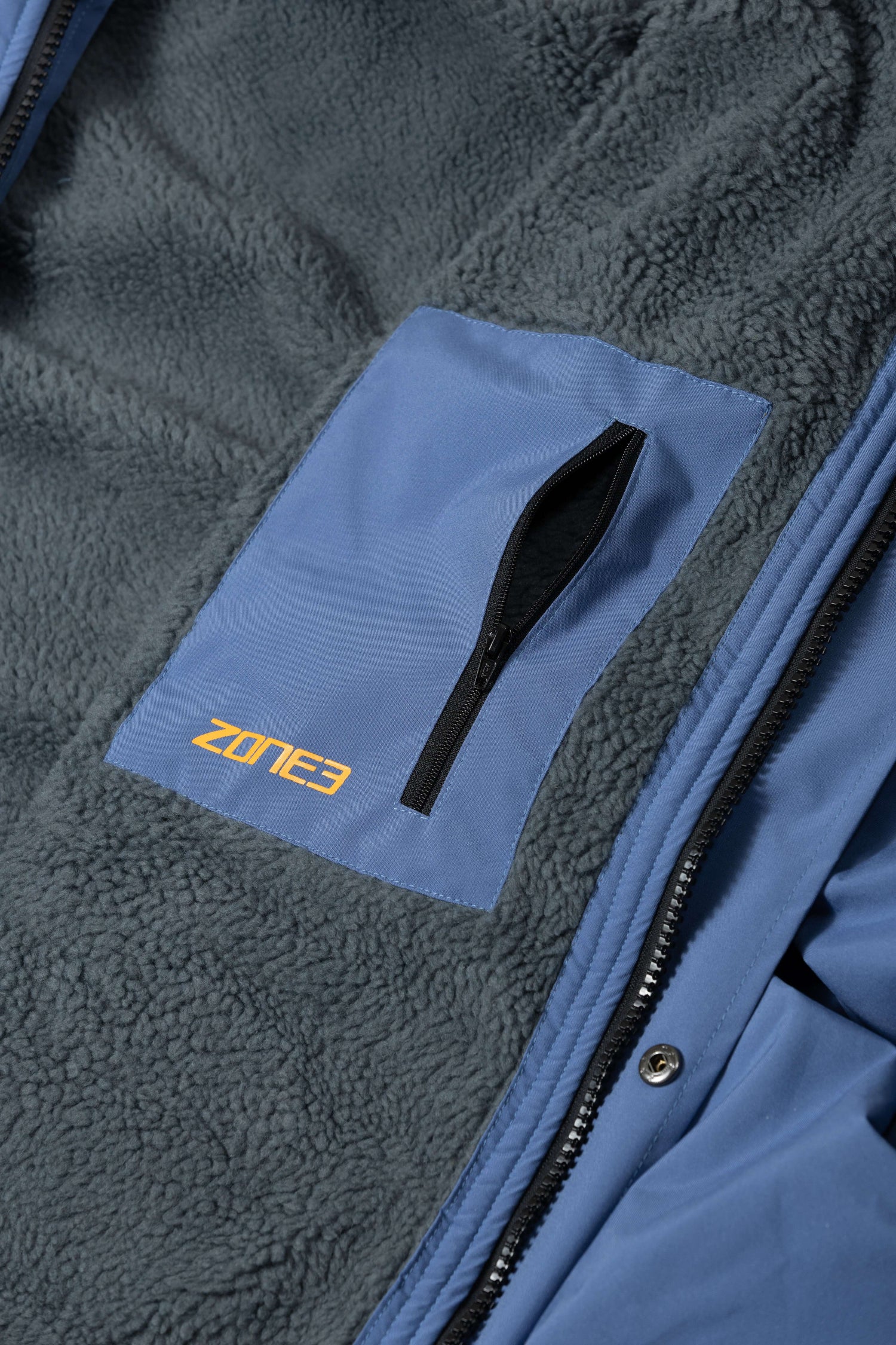 Primer plano del bolsillo interior con cremallera en el pecho, sobre el forro polar, bordado con el logotipo de ZONE3.