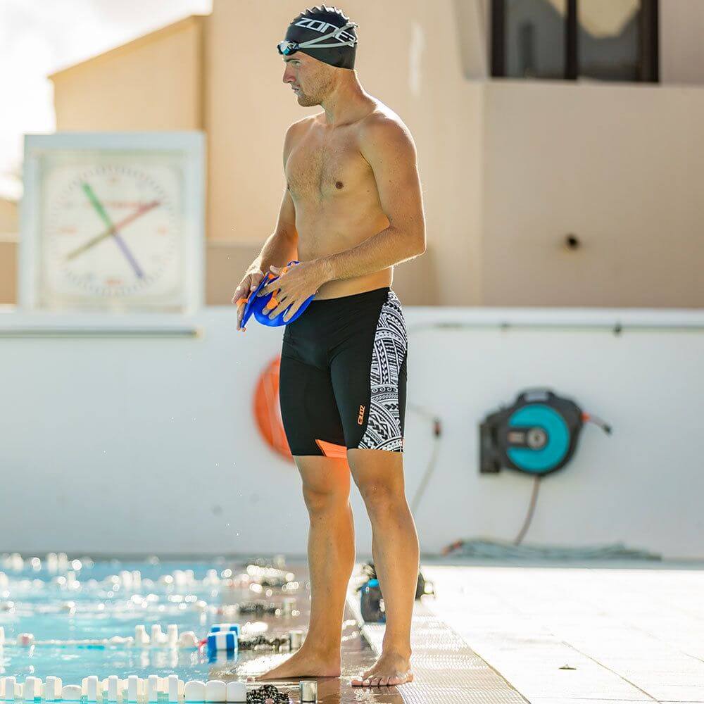 Hombre junto a la piscina con el jammer de natación negro, estampado Kona Speed en blanco en el lateral y detalles naranjas.